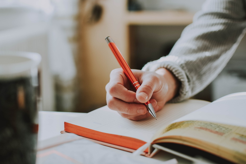 human hand, publication, page, close-up, focus, handwritten, hand, focus on foreground, one person, table, note pad, pencil, pen, depth of field, orange