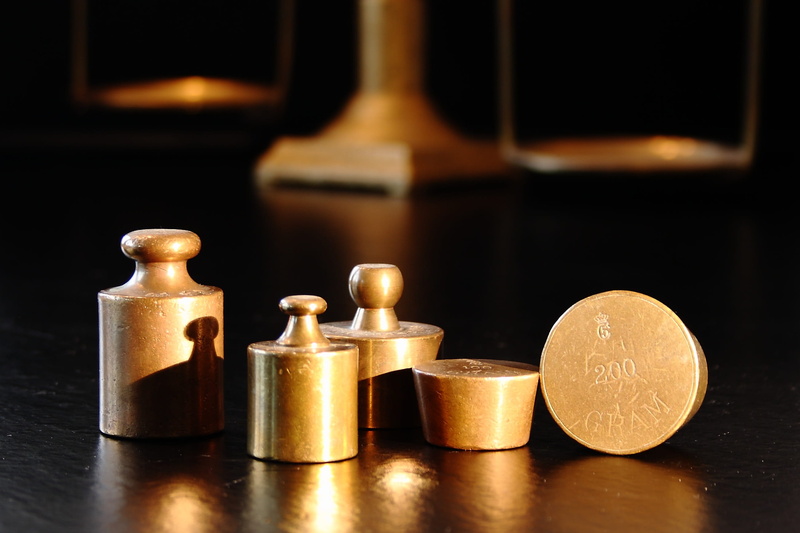 gold colored, studio shot, arrangement, weights, group of objects, brass, simplicity, balance, black background, table, focus on foreground, indoors, close-up