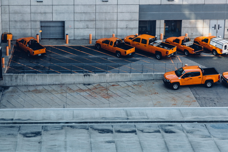 tractor, building exterior, motor vehicle, car, traffic, orange, outdoors, parking lot, city, architecture, parking, orange color, built structure, cab