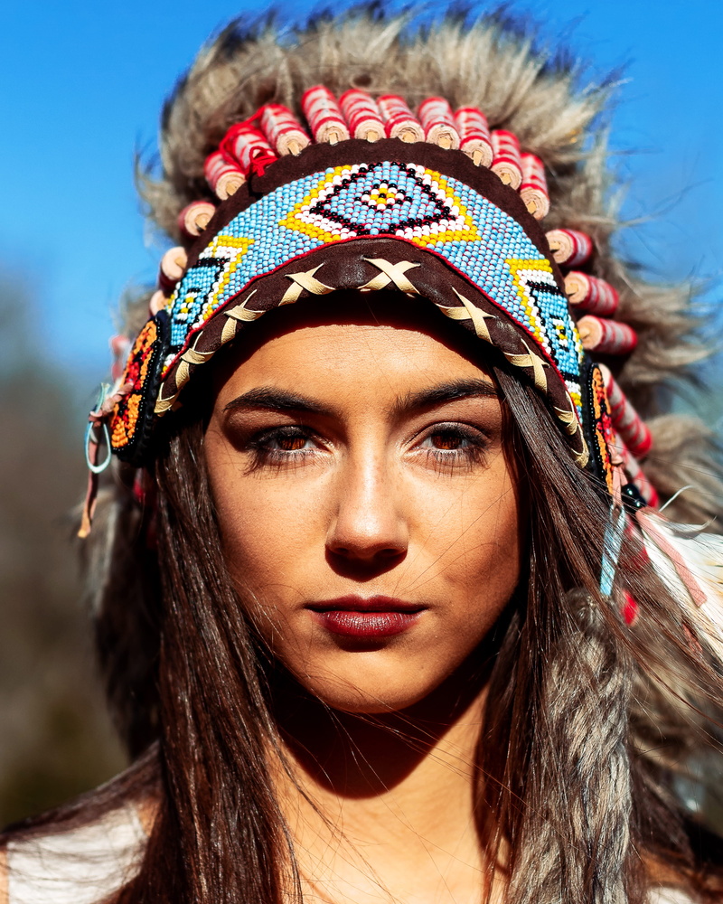 spirit, headdress, sunlight, hair, focus on foreground, hairstyle, trees, portrait, long hair, beauty, headshot, eyes, contemplation, lifestyles, adult