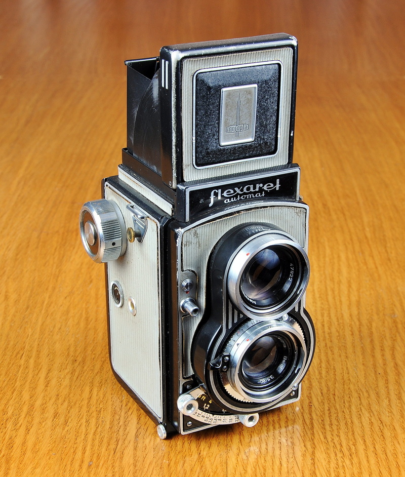 single object, table, brand camera, indoors, flexaret, twin-lens reflex camera, chrome, retro styled, no people, man made object, silver colored, antique