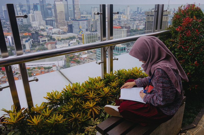 three quarter length, outdoors, cityscape, bench, clothing, woman, sweatshirt, person, city, balcony, jakarta, architecture, building, built structure