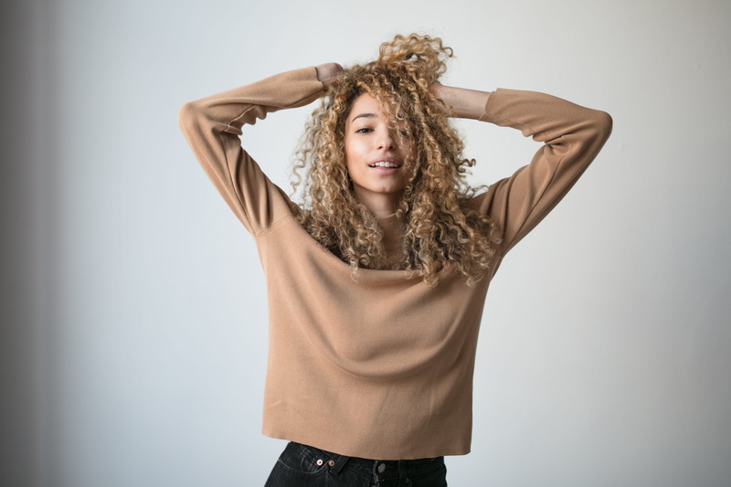person, long, wall, hand in hair, blond hair, smiling, top - garment, hair, s, long hair, near, woman, blouse, sweater, one person, front view, beautiful woman
