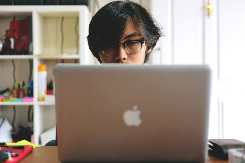 near, using laptop, macbook, adult, silver, eyeglasses, concentration, sitting, man, computer, shelf, room, wooden, table, business, connection, laptop