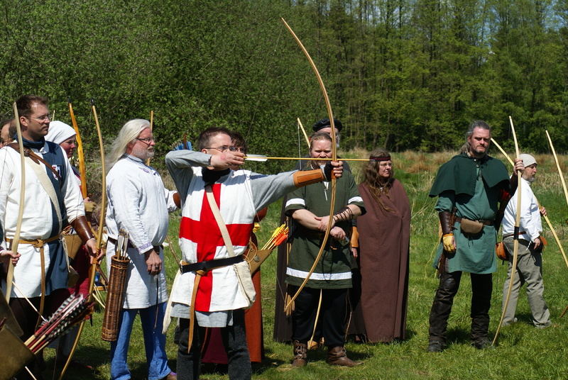 casual clothing, teamwork, cooperation, artist, outdoors, arch, tree, archery, holding, music, plant, weapon, group of people, arts culture and entertainment