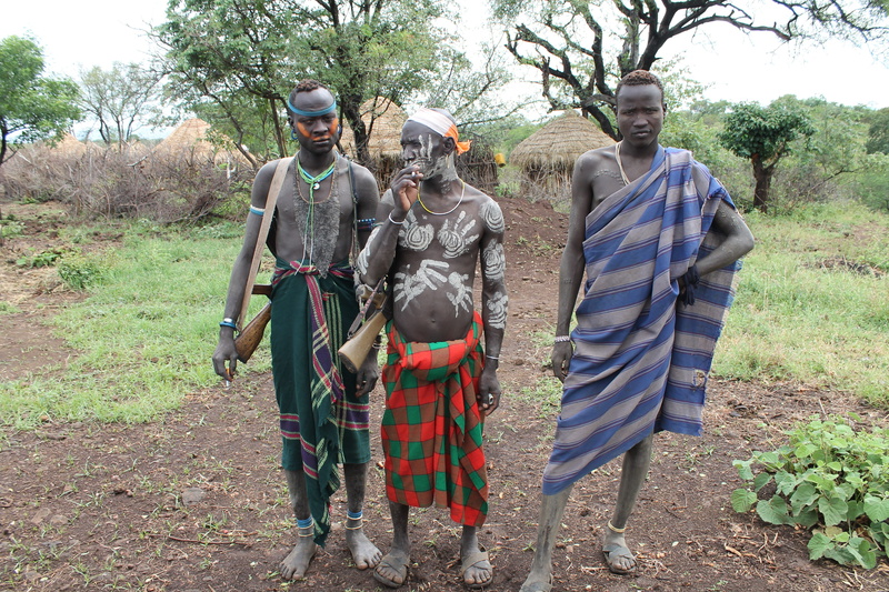 day, traditional clothing, lifestyles, real people, people, clothing, black skin, land, Mursi, walking, Warriors, tree, rear view, plant, adult, outdoors