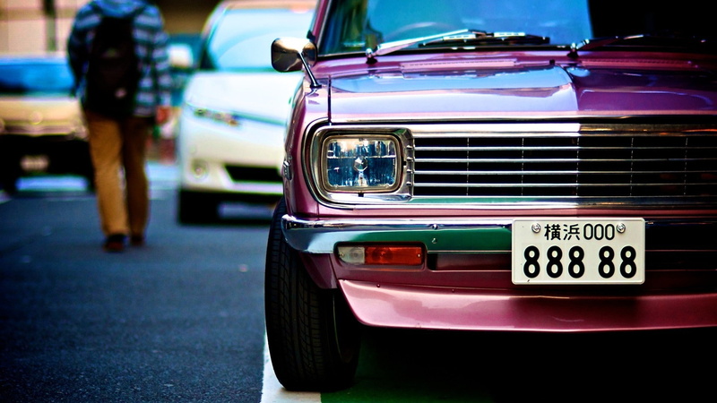 focus on foreground, Datsun, close-up, architecture, western script, land vehicle, street, day, transportation, text, outdoors, incidental people, headlight
