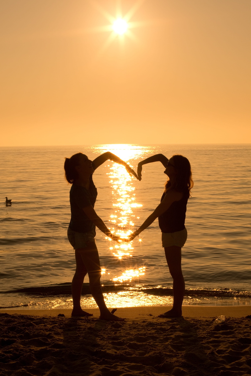 real people, horizon over water, beauty in nature, lens flare, lifestyles, hour, sea, silhouette, heart, women, sky, beach, standing, horizon, sun, two