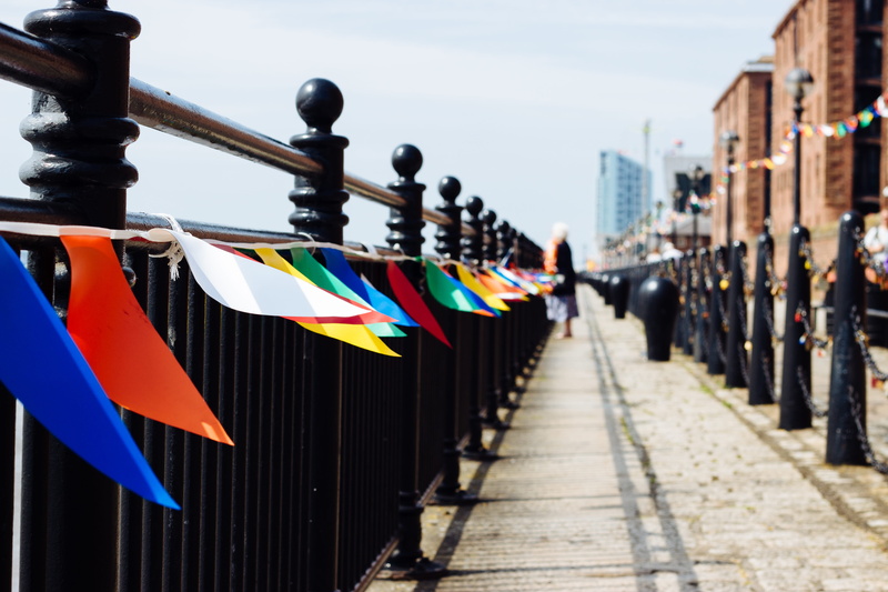 5K, flags, day, building exterior, footpath, waterfront, built structure, street, outdoors, focus on foreground, hanging, direction, railing, multi colored