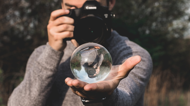 holding, outdoors, tree, human body part, technology, globe, space, one person, day, hand, nature, blur, camera - photographic equipment, sphere, looking