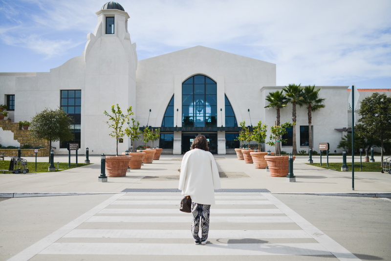 street, top, coat, palm trees, airport, one person, pedestrian, full length, woman, built structure, belief, sidewalk, plants, lifestyles, jacket, women