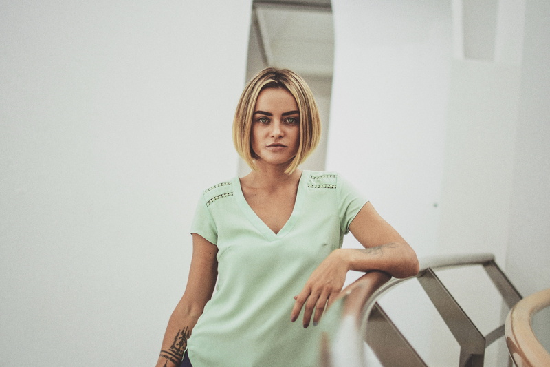 person, portrait, blond hair, casual clothing, female, evening, cafe, leaning on, mid adult, front view, standing, room, looking at camera, near, rail