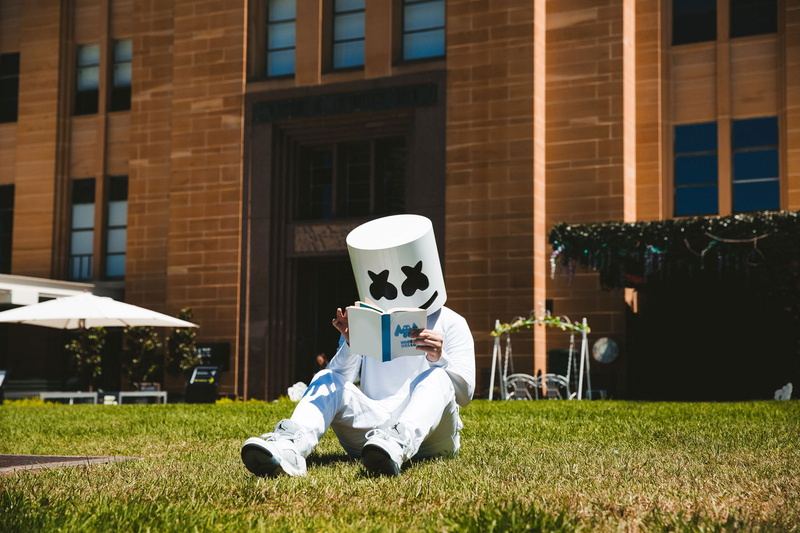 real people, sitting, dj, singer, one person, day, leisure activity, outdoors, marshmello, nature, grass, building exterior, full length, men, plant, architecture