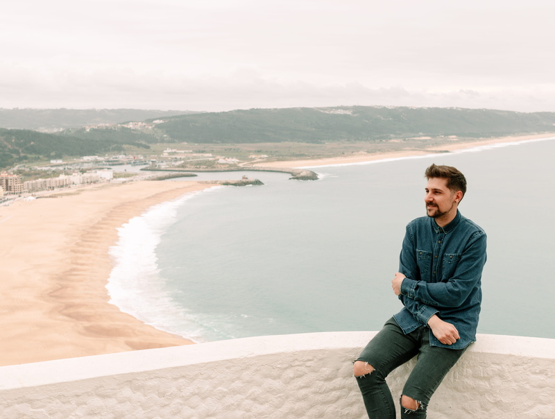 leisure activities, sitting on ledge, portrait, young adult, sea shore, standing, real people, man, nazaré, one person, human, ocean, beach, scenics - nature