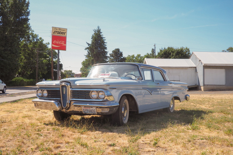 sign, retro styled, communication, road, sedan, grass, car, tent, mode of transportation, nature, parking, teal, sunlight, plant, outdoors, brown, stationary
