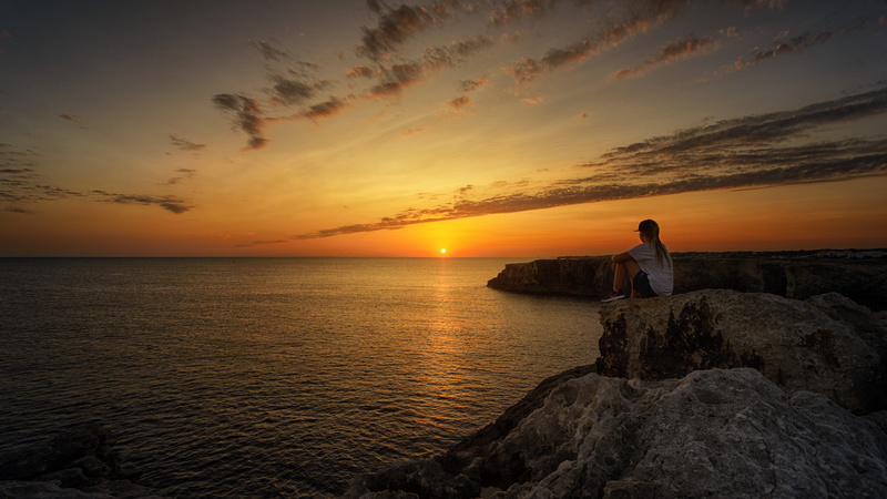 sitting, waters, looking at view, summer, water, girl, land, beach, outdoors, contemplation, one person, rock, person, beauty in nature, cloud - sky, sunset