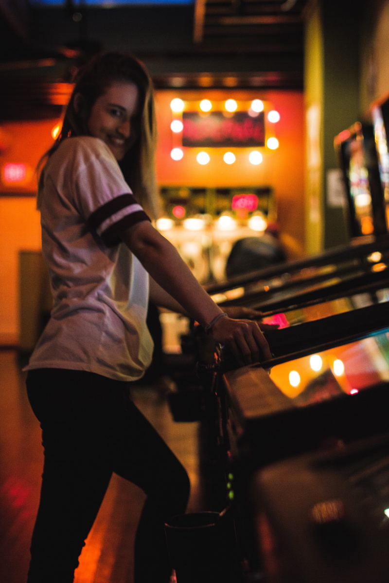 arts culture and entertainment, real people, young women, girl, focus on foreground, hairstyle, pinball, nightlife, smile, entertainment occupation, standing