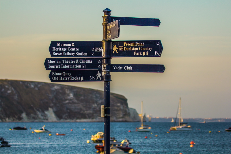 pole, sign, information sign, focus on foreground, arrow symbol, sea, sky, text, transportation, western script, outdoors, nature, no people, water, swanage bay