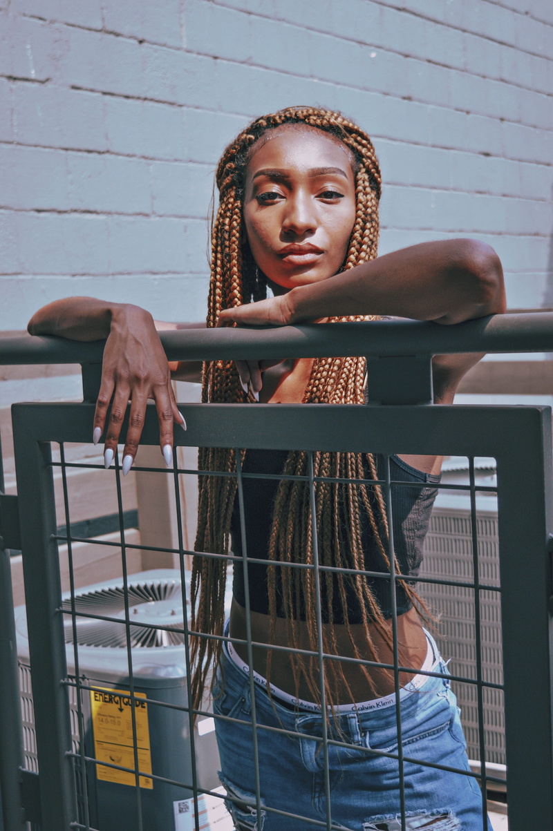 finger, head, beautiful woman, metal, casual clothing, wall - building feature, neck, outdoors, woman, frame, standing, hairstyle, person, day, looking