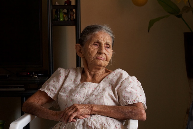 waist up, woman, you vejes, front view, indoors, 5K, time, elder, looking at camera, women, dress, chair, gray hair, white, sitting, contemplation, senior women