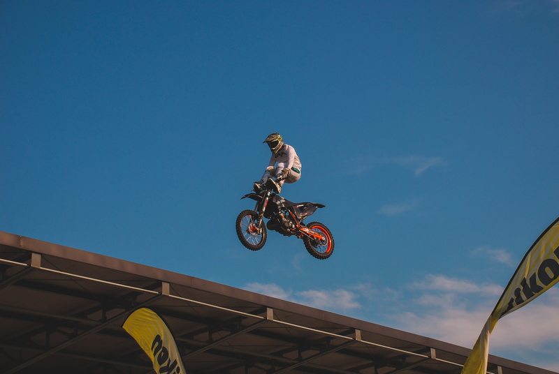lifestyles, mode of transportation, jumping, sky, low angle view, motocross, headwear, roof, blue, ramp, jump, motorcycle, motion, mid-air, outdoors, car