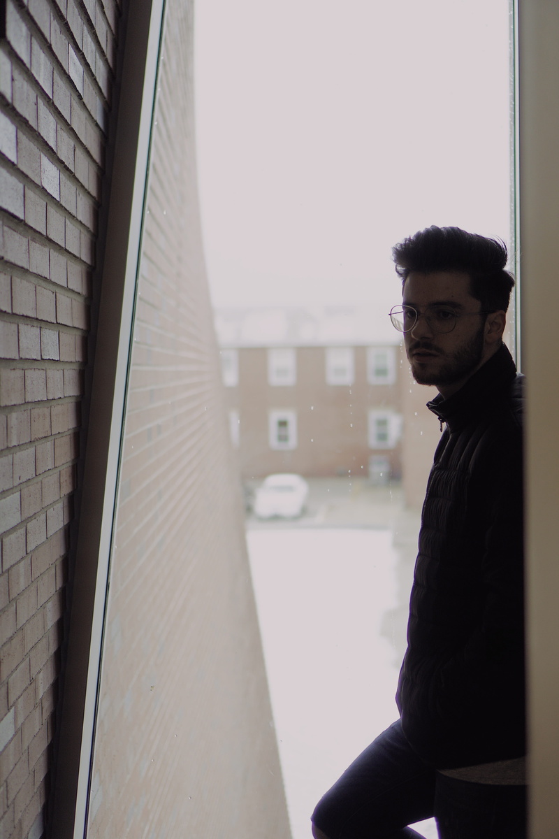 one person, winter, building exterior, man, waist up, black, leaning, jacket, contemplation, day, young men, casual clothing, lifestyles, window, side view