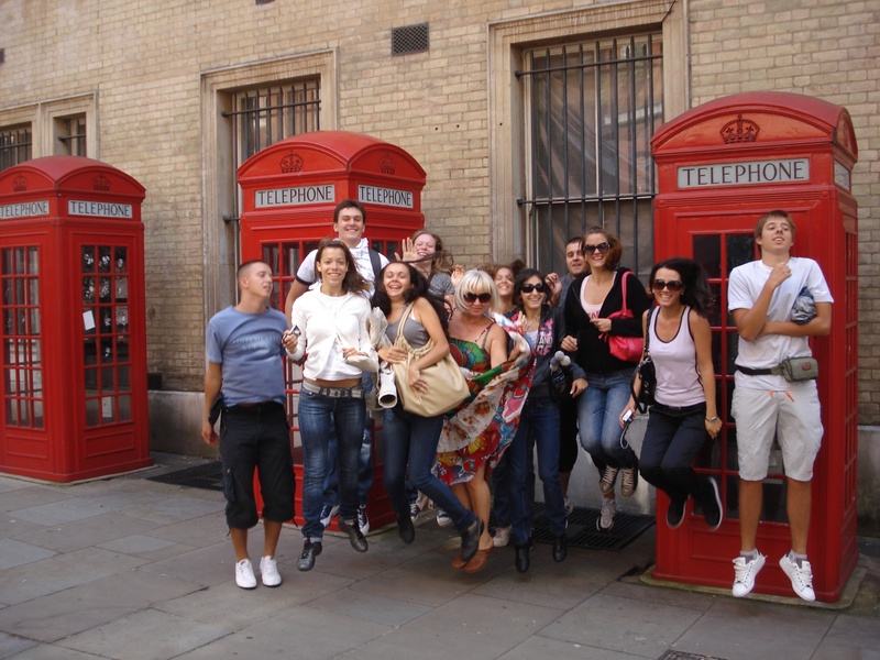 looking at camera, booths, young adult, togetherness, building exterior, 2K, building, males, near, full length, telephone, english, students, smiling