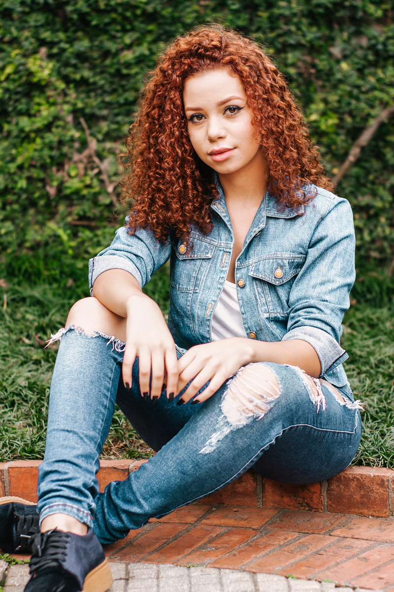 fashion, looking at camera, lifestyles, portrait, curly hair, cute, denim pants, young adult, young women, one person, redhead, seated, front view, women