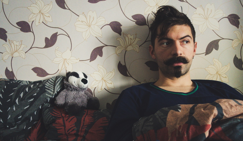 boy, floral pattern, bedroom, leisure activity, raccoon, contemplation, real people, 5K, facial hair, young man, representation, indoors, young men, blanket