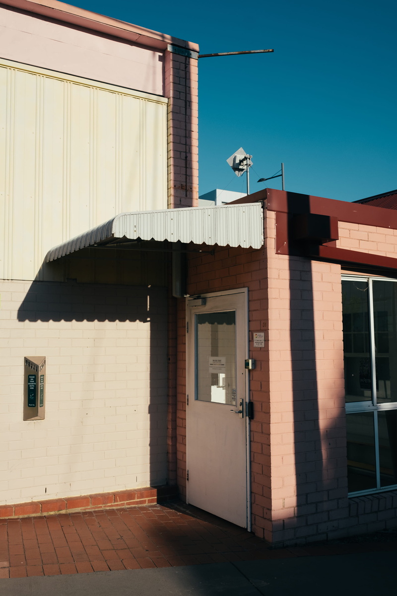 blue, street, clear sky, brown, suburbia, wall, white, brick, roof, building exterior, sky, architecture, shadow, city, building, pink, sunlight, postal office