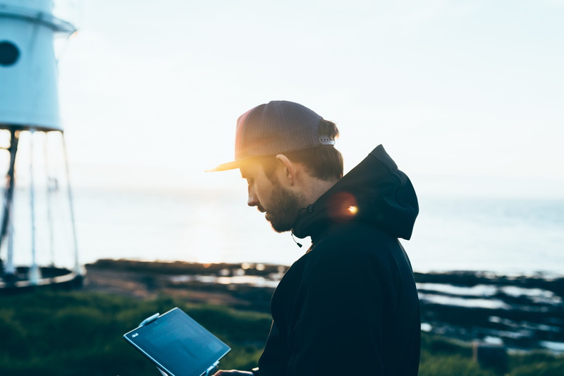 sun, young adult, blur, real people, focus on foreground, sunlight, water, people, standing, nature, gadget, lens flare, sea, day, sky, travel, ocean, tablet