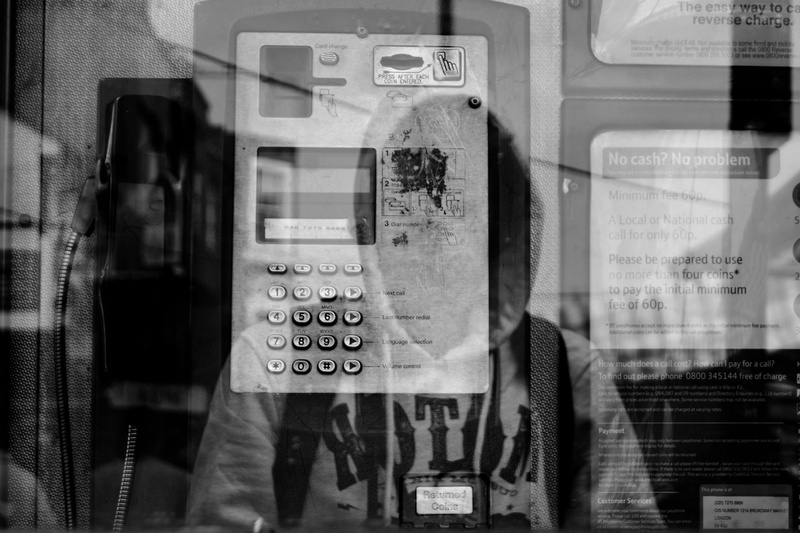 photo, suburban, built structure, glass - material, booth, day, grayscale, man, wearing, wall, one person, telephone receiver, number, telephone, pay phone