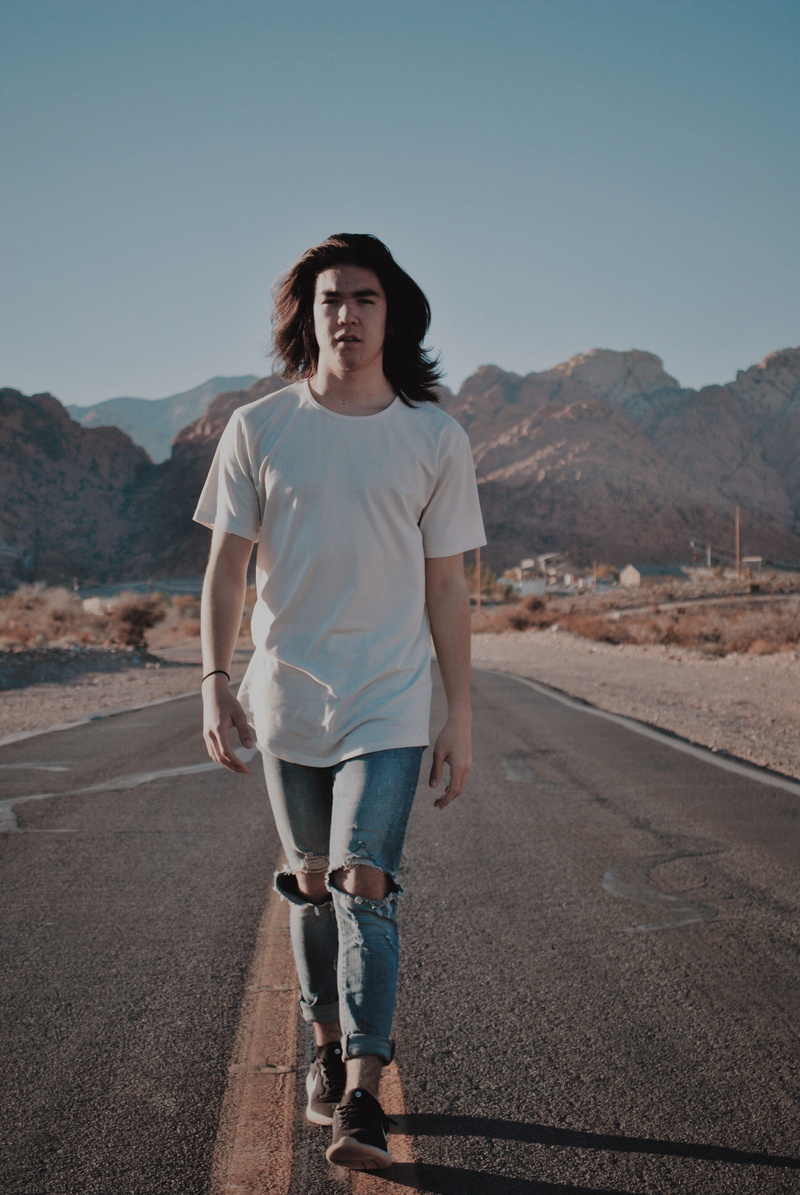 walking, tarmac, hat, t-shirt, front view, road, mountain, riding boot, sky, transportation, looking at camera, nature, real people, lifestyles, boot, young adult