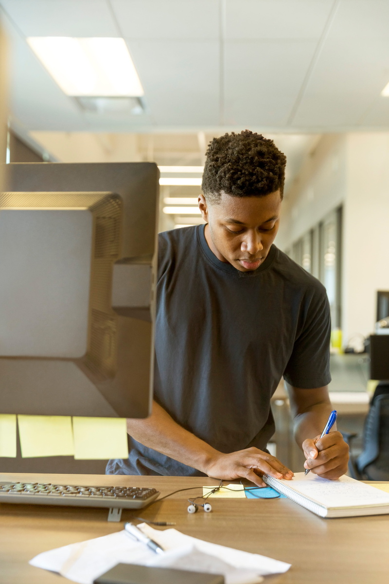real people, table, young men, indoors, office, looking, modern, looking down, working, one person, notebook, casual clothing, computer, waist up, document