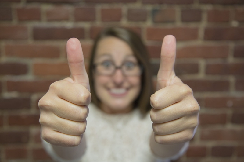 thumb, headshot, aggression, portrait, smiling, woman, adult, human arm, gesture, front view, marketing, top, gestures, brick wall, gesturing, human body part