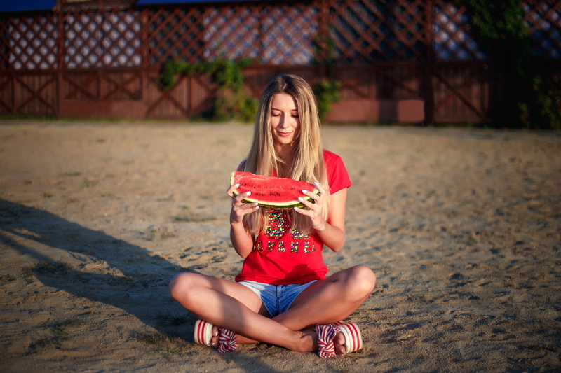 painted nails, watermelons, sitting, jean shorts, women, food, on the floor, portrait, depth of field, model, smiling, blonde, T-shirt, 2K, legs crossed