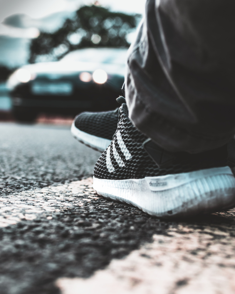 headlights, car, blur, warm clothing, footwear, surface level, sneakers, white, person, adidas, human body part, human limb, wear, mode of transportation