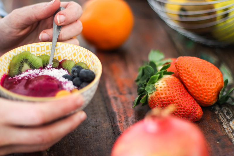 person, acai bowl, mixed, one person, human hand, bowl, table, sliced, crockery, breakfast, food, fruits, blueberry, yellow, adult, salad, preparation