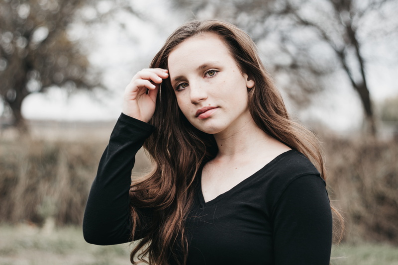 hair, focus on foreground, looking at camera, photo, one person, teen, standing, kid, front view, quiet, beautiful woman, tree, young women, touching, face
