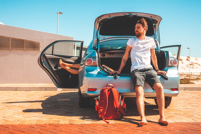 man, day, shadow, motor vehicle, car wheel, car, wheel, bag, machine, car trunk, wood, shorts, person, full length, alloy wheel, sitting, plywood, real people