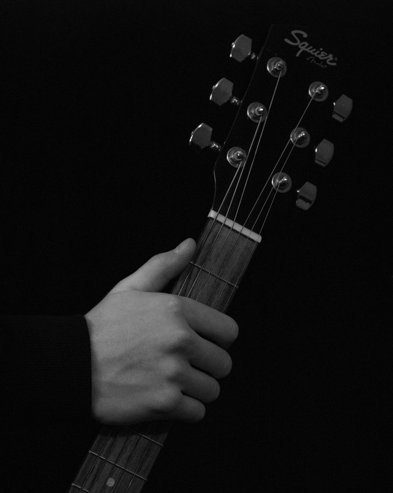 acoustic guitar, holding, close-up, black background, person, indoors, black, human body part, instrument, fender, black and white, one person, classic