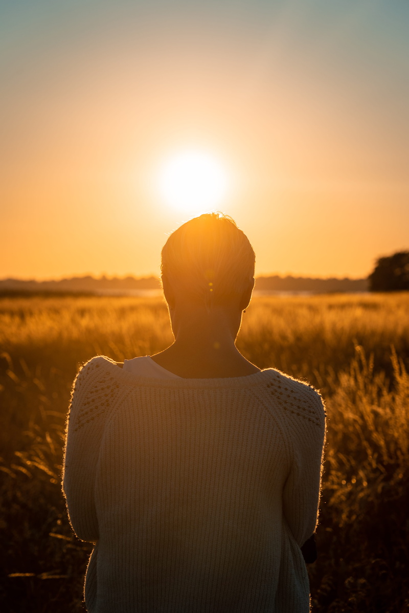 dusk, orange color, casual clothing, hairstyle, waist up, sunset, person, beauty in nature, one person, lens flare, sitting, glow, field, sun, leisure activity