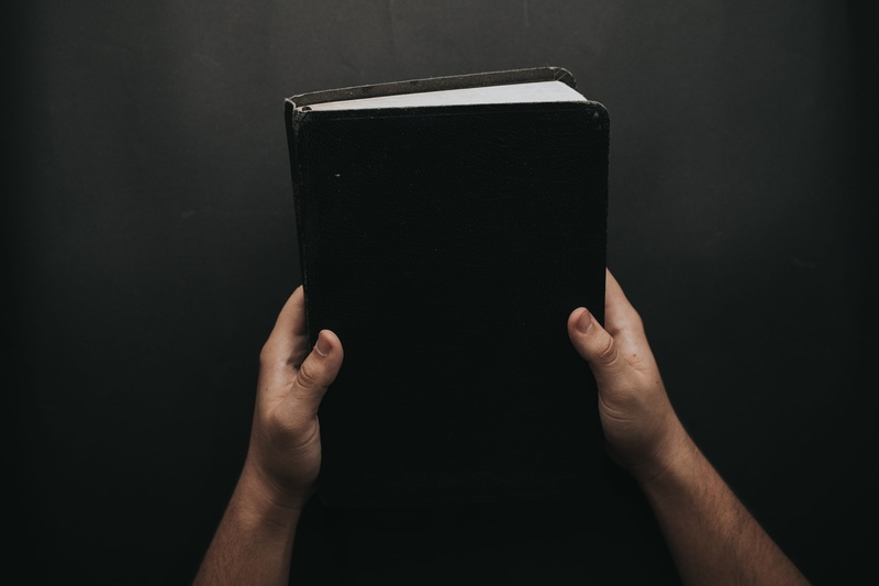 bible, book, one person, wireless technology, person, human hand, lifestyles, single object, 5K, black, cover, studio shot, human body part, portable information device