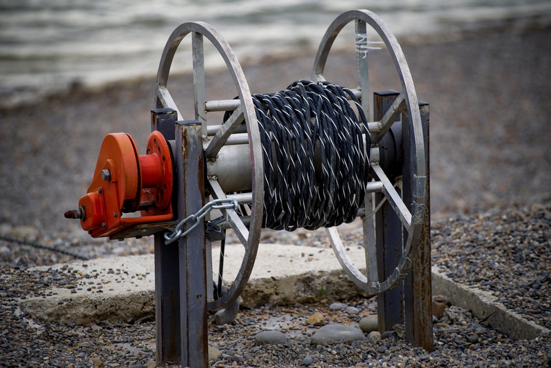 cable, cord, sunlight, boat, lake, manual, metal, spool, absence, rope, focus on foreground, sand, water, 5K, outdoors, equipment, day, no people, land