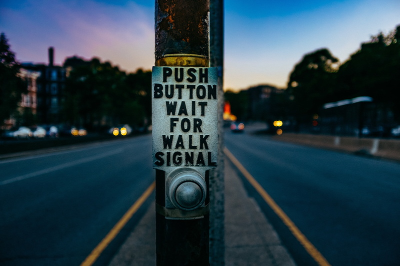 focus on foreground, guidance, signal, building exterior, inscription, push button, text, car, city, outdoors, street, button, sunset, no people, walk